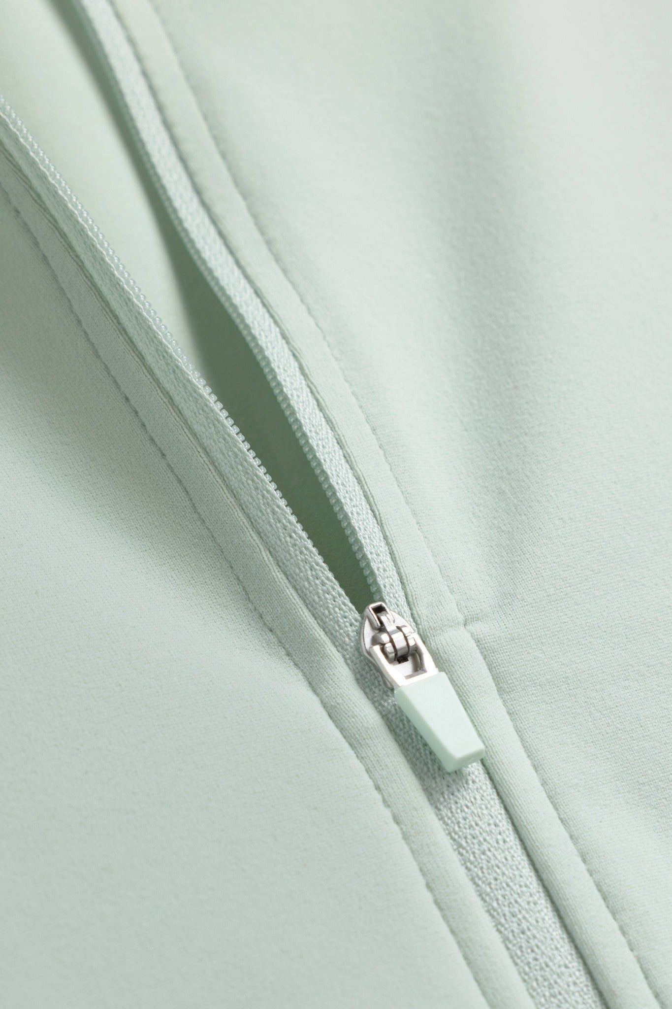 Close-up of the zipper detail on the CASPARA Sculptluxe zip jacket in pistachio green.